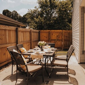 An outdoor patio with a wooden table set for dining, surrounded by wicker chairs with cushions. - Savannah Oasis 10min to Beach + Historic Downtown (Savannah)