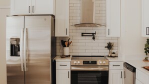 A modern kitchen with stainless steel appliances, white cabinetry, and a tiled backsplash.