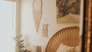 A bedroom with a bed, a nightstand, a lamp, a wall hanging, and a window with a plant.