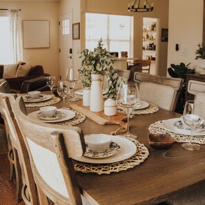 A dining table set with white plates, bowls, and wine glasses, surrounded by wooden chairs. - Savannah Oasis 10min to Beach + Historic Downtown (Savannah)