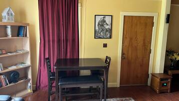 Un comedor con una mesa y sillas de madera, una estantería, una cortina roja, un cuadro enmarcado en la pared y una puerta de madera.