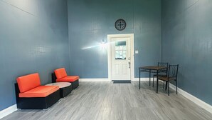 Een kamer met blauwgroene wanden, een houten plafondventilator, een deur met ruit en een kleine tafel met stoelen.