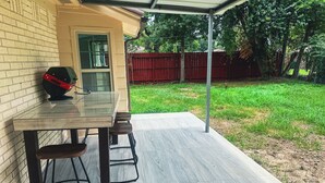 Een terras buiten met een tafel en stoelen, een barbecue en een rode omheining op de achtergrond.