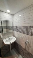 Un baño con lavamanos blanco, un espejo y ducha.