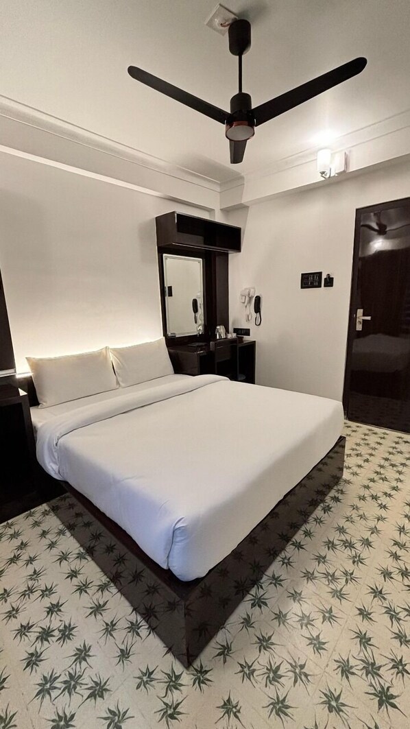 A hotel room with a bed, a ceiling fan, a mirror, a telephone, and a door.