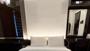 A hotel room with a large bed, a nightstand, a mirror, and a dresser. - LUXESTYLE (Adoor)
