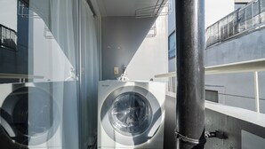 A compact, modern laundry room with a front-loading washing machine and a dryer, enclosed by glass walls and a metal railing. - Excellent access to Shibuya area! Residence with cherry blossom motif [307]. (Meguro-ku)