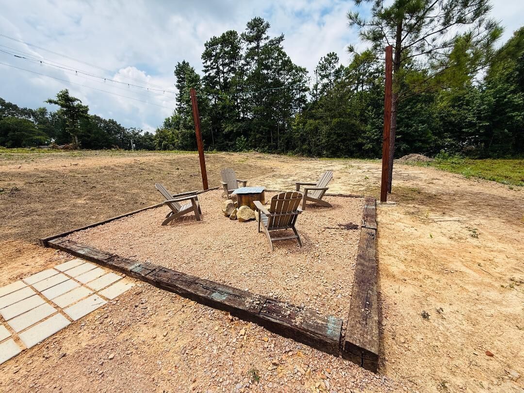 An outdoor seating area with a table and chairs, surrounded by a wooden fence and trees in the background.