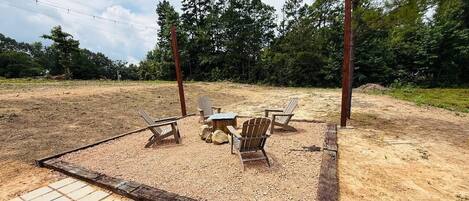 An outdoor seating area with a table and chairs, surrounded by a wooden fence and trees in the background.