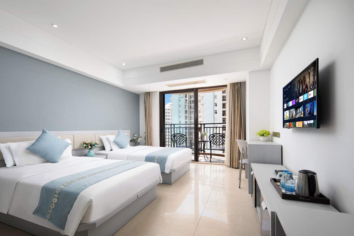 A modern hotel room with two beds, a balcony, a TV, and a desk with a coffee maker.