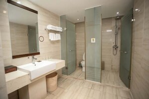 Une salle de bain moderne avec un grand miroir, un lavabo blanc, une douche en verre et des toilettes.