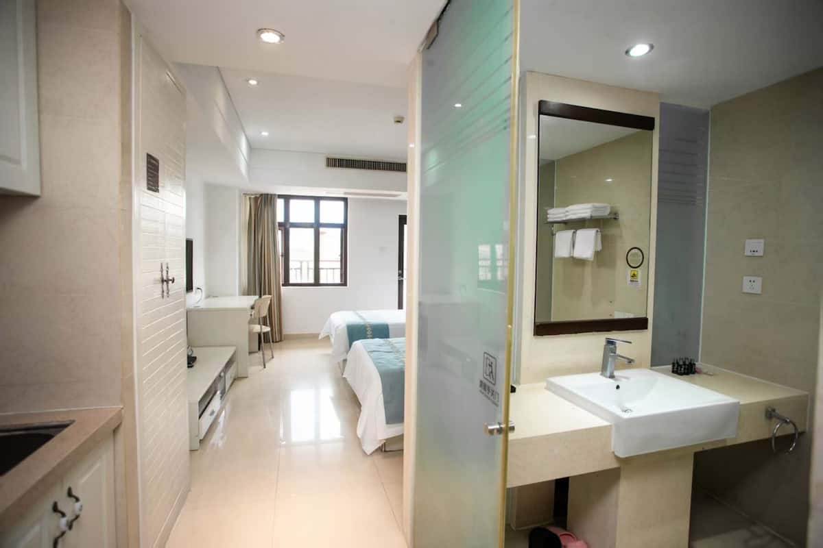 A hotel room with a kitchenette, a large mirror, a sink, and a bed with a blue bedspread.