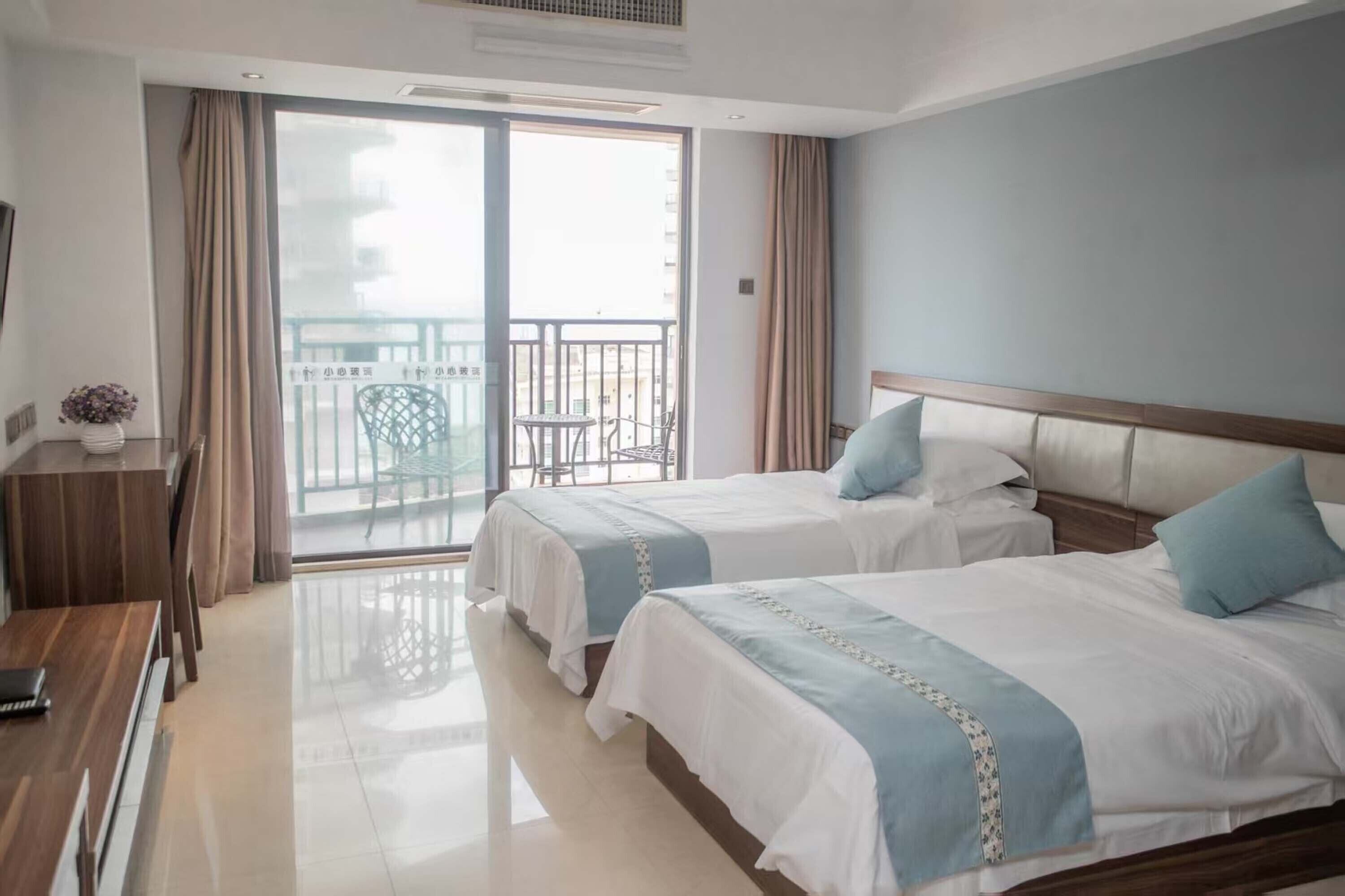 A hotel room with two beds, a desk, a chair, and a balcony with a view.