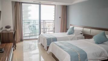 A hotel room with two beds, a desk, a chair, and a balcony with a view.