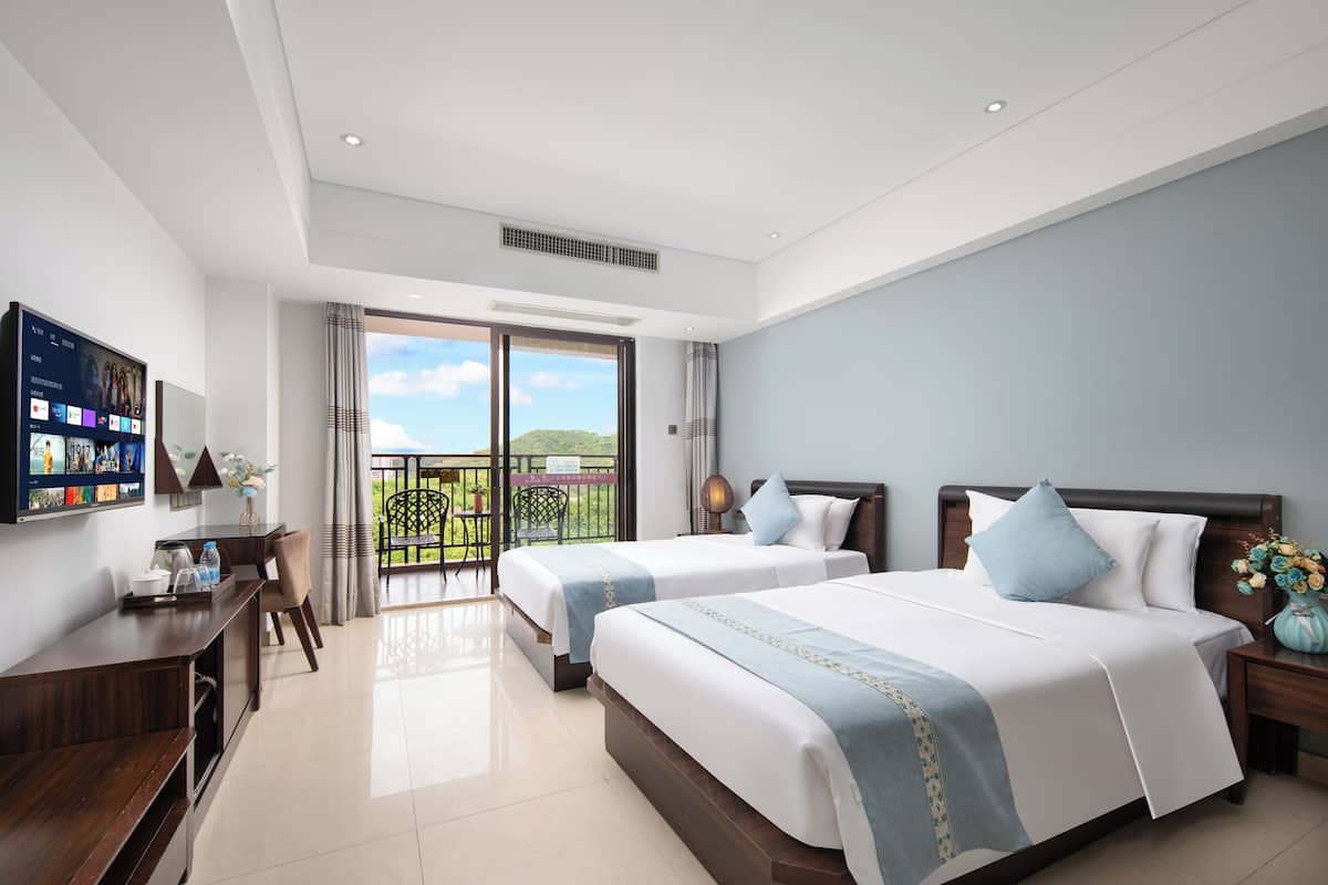 A hotel room with two beds, a desk, and a balcony with a view.