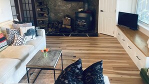 A modern living room with a stone fireplace, wooden flooring, a sofa with patterned cushions, and a TV on a wooden cabinet. - A restful stay in Georgian Bluffs (Georgian Bluffs)
