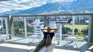 A man relaxing on a bench with a city and mountains in the background.