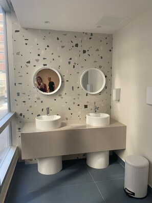 Ein modernes Badezimmer mit zwei Waschbecken, einem großen Spiegel und einem Mülleimer.
