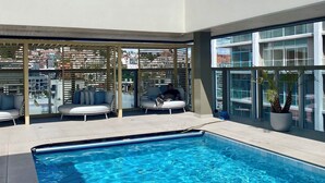 A modern hotel with a rooftop pool, outdoor seating, and a view of the cityscape.
