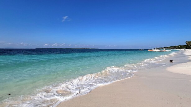 A beach with clear turquoise water, a sandy shore, and a boat in the distance. - Bara Cabana Hotel (Bira)