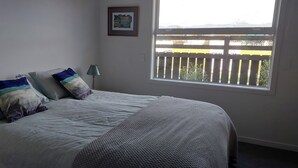 A bedroom with a bed, pillows, a nightstand, a lamp, a window, and a framed picture on the wall. - Kotuku - a quiet retreat in lovely Mapua (Māpua)