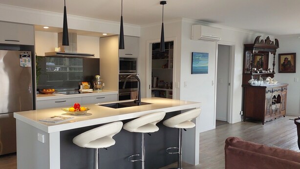 A modern kitchen with a central island, bar stools, a refrigerator, and a microwave. - Kotuku - a quiet retreat in lovely Mapua (Māpua)
