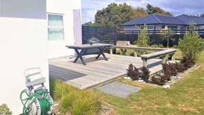 A patio area with a table and benches, surrounded by a garden with various plants and a hose. - Kotuku - a quiet retreat in lovely Mapua (Māpua)