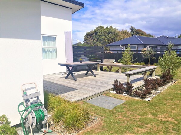A patio area with a table and benches, surrounded by a garden with various plants and a hose. - Kotuku - a quiet retreat in lovely Mapua (Māpua)