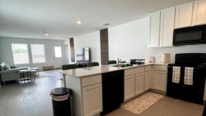 Een moderne keuken met witte kasten, een zwart fornuis en een zithoek met een bank en tafel.