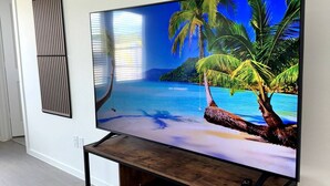 Een flatscreen televisie op een houten tv-meubel in een kamer met witte wanden en een houten vloer.