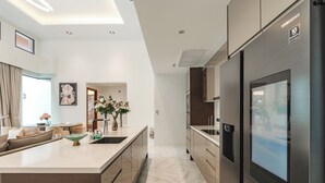 Una cocina moderna con un refrigerador de acero inoxidable grande, una encimera de mármol y una zona de comedor con sofá y mesa.