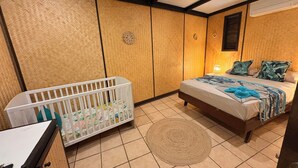 Ein Schlafzimmer mit einem Kinderbett, einem Bett mit gemustertem Überwurf, einem gewebten Teppich und einer Wand-Klimaanlage.