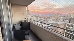 A balcony with wicker furniture, a small round table, and a cityscape view during sunset. - Centrally located apartment, fully equipped, with beautiful terrace, steps from the Metro. (Santiago)