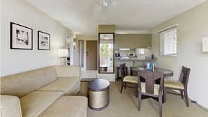 Una sala de estar con un sofá, una mesa de centro y un comedor con una mesa y sillas. Se ve un área de cocina a través de una puerta abierta.