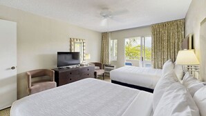 Habitación de hotel con dos camas, televisor, cómoda y balcón con cortinas.