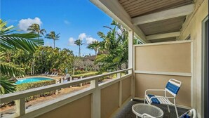 Un balcón con vistas a una piscina, rodeado de palmeras y un cielo azul despejado.