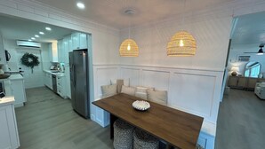 A modern kitchen with white cabinetry, a stainless steel refrigerator, and a wooden dining table with woven stools. - Key Largo 3 bedroom 2 bathroom home with spacious lot for boat/RV parking (Key Largo)