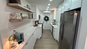 A narrow kitchen with white cabinets, a stainless steel refrigerator, and a small island with a lamp. - Key Largo 3 bedroom 2 bathroom home with spacious lot for boat/RV parking (Key Largo)