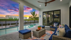 Un patio moderno al aire libre con piscina, mobiliario de mimbre y vistas al atardecer.