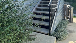 Un escalier menant à un balcon agrémenté de rampes en métal, le tout entouré de verdure.