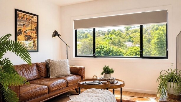 Un salon moderne avec un canapé en cuir, une table basse ronde, une grande fenêtre donnant sur un paysage verdoyant et un tableau encadré accroché au mur.
