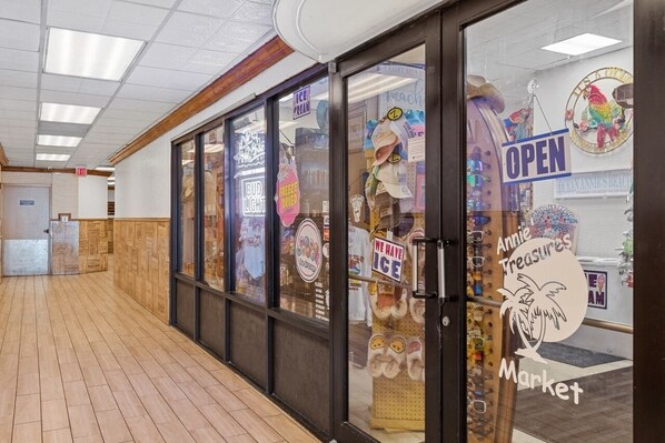 A corridor with wooden flooring, glass doors to a market, and various signs advertising ice cream and other items.