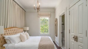 A large, neatly made bed with a headboard, a chandelier, and a window with curtains. - Mirabelle Suite 2 - Private Suite in Historic Savannah (Savannah)