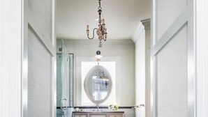 A narrow hallway with a vanity, a round mirror, and a chandelier.