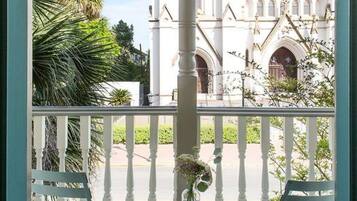 A balcony with two white chairs and a white table with a vase of flowers. A white building with a large circular window and arched windows is visible in the background.