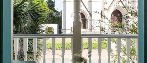 Un balcon avec deux chaises blanches et une table blanche ornée d’un vase de fleurs. On aperçoit, en arrière-plan, un bâtiment blanc doté d’une grande fenêtre circulaire et de fenêtres en arc de cercle.
