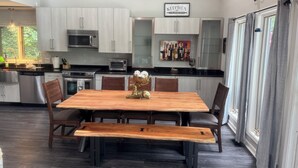 Una cocina moderna con armarios de madera clara, electrodomésticos de acero inoxidable y una zona de comedor con mesa y bancos de madera.