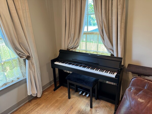 A piano in a room with wooden flooring, a bench, and curtains.