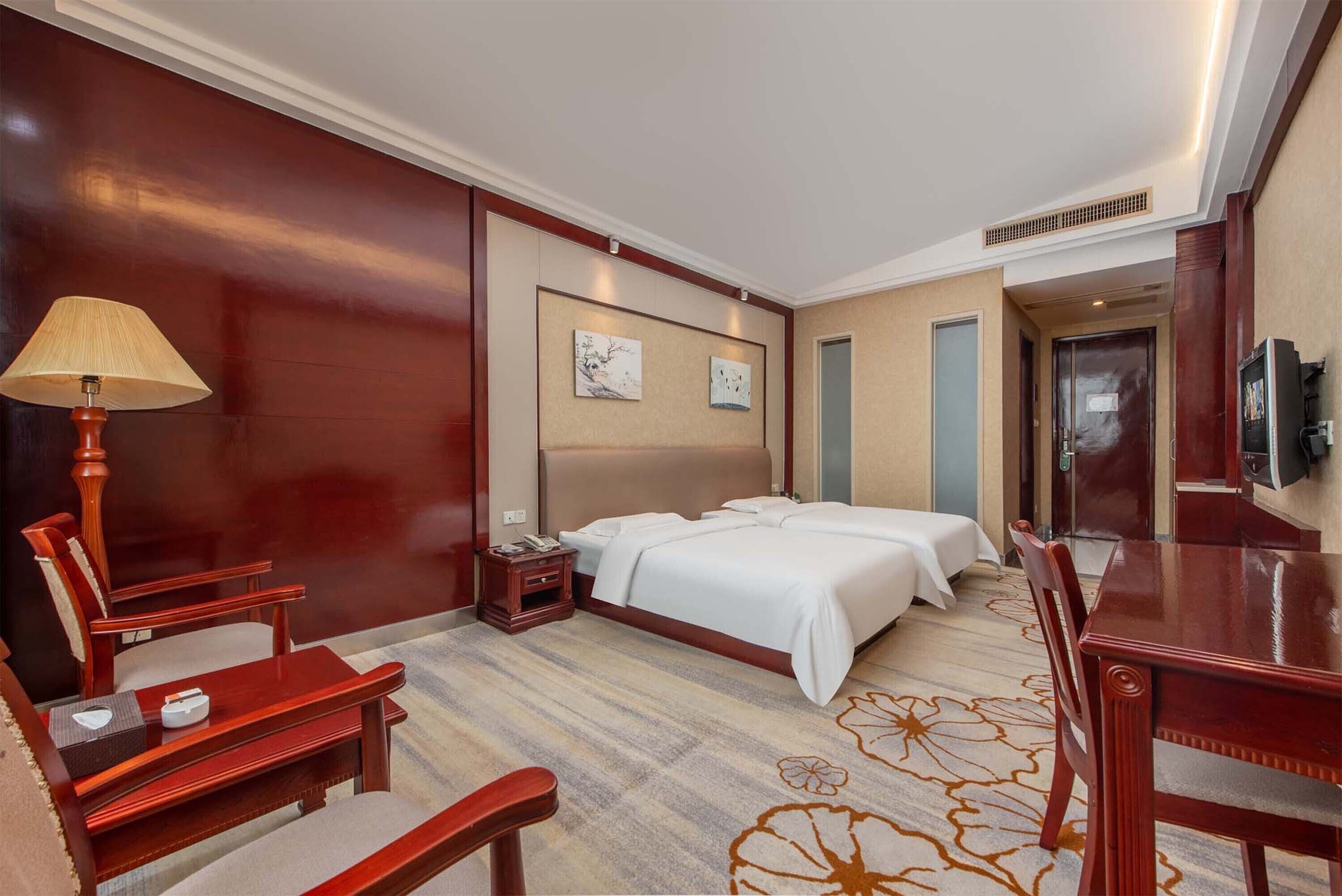 Une chambre d’hôtel comprenant un lit, deux tables de chevet, un bureau, une chaise, une lampe et un téléviseur.