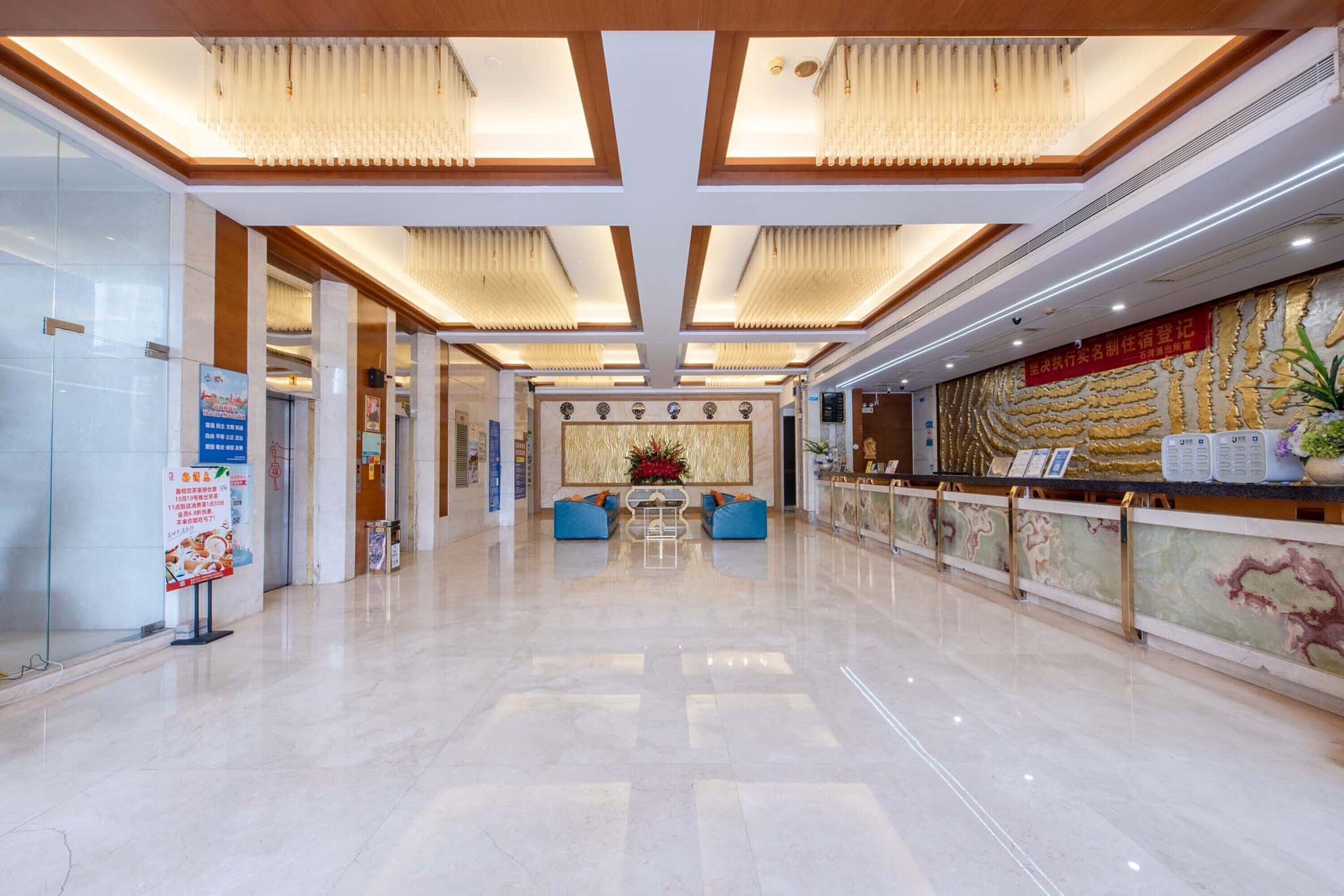 A spacious lobby with a polished marble floor, a reception desk, and a seating area with blue sofas.